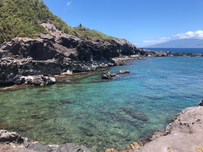 白天，蓝天下蓝海旁的绿色和棕色山
